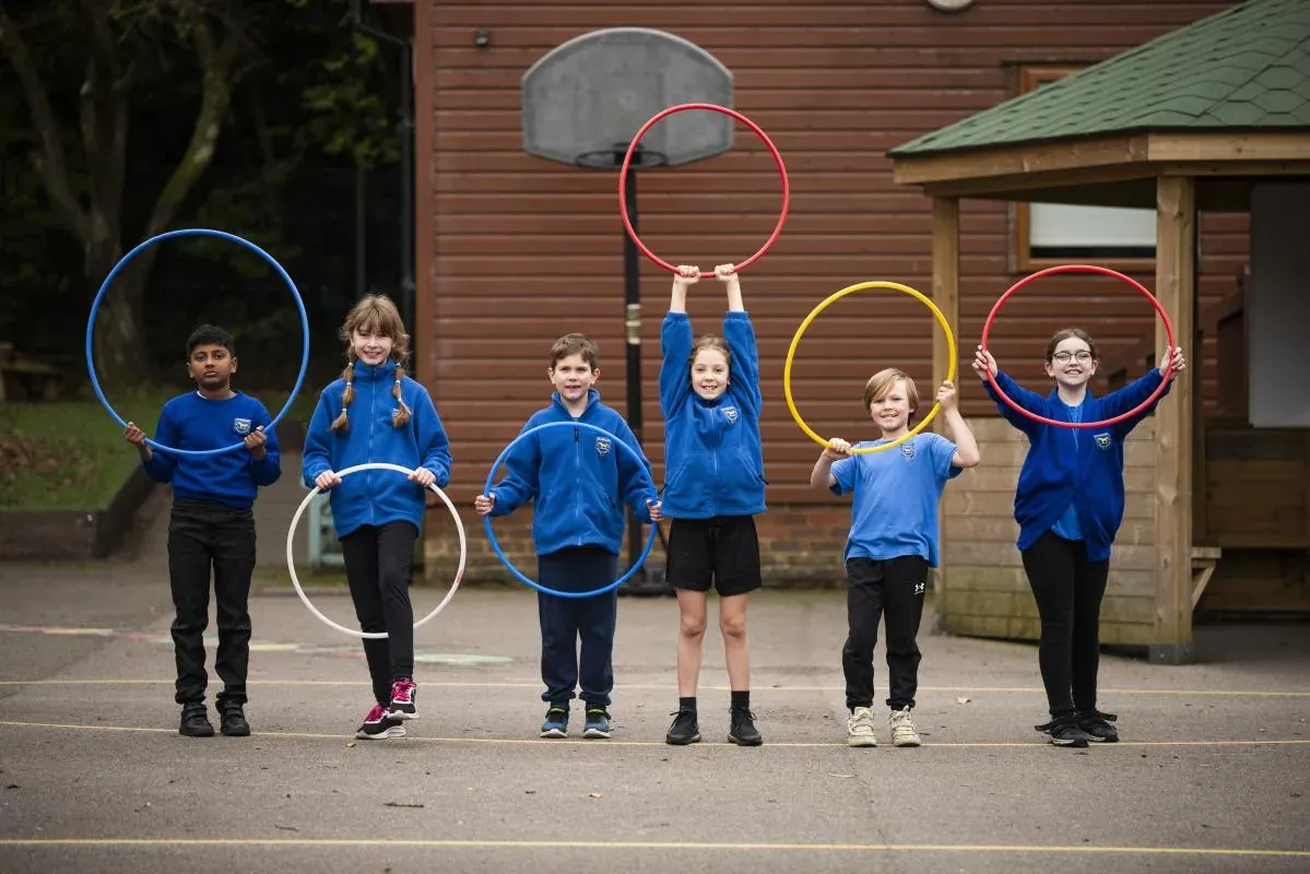 Pupils in royal-blue school fleeces holding coloured hoops in the playground
