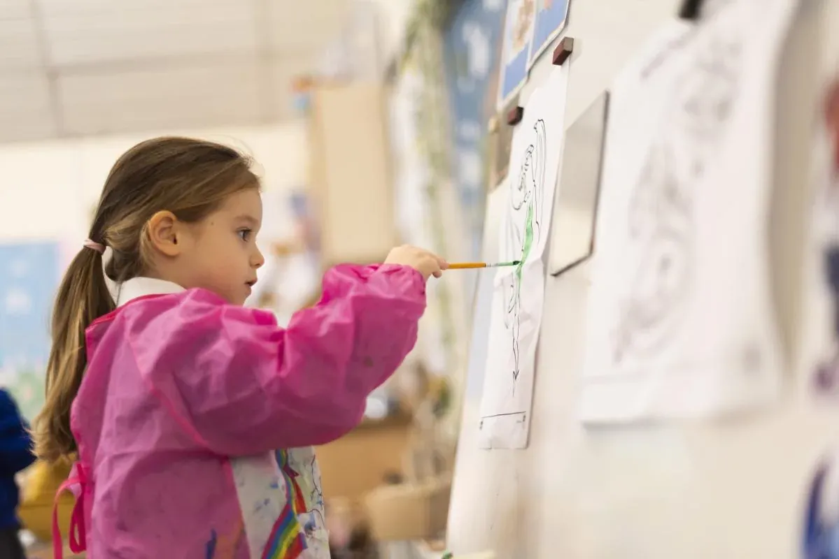 A girl in a pink apron painting at an easel